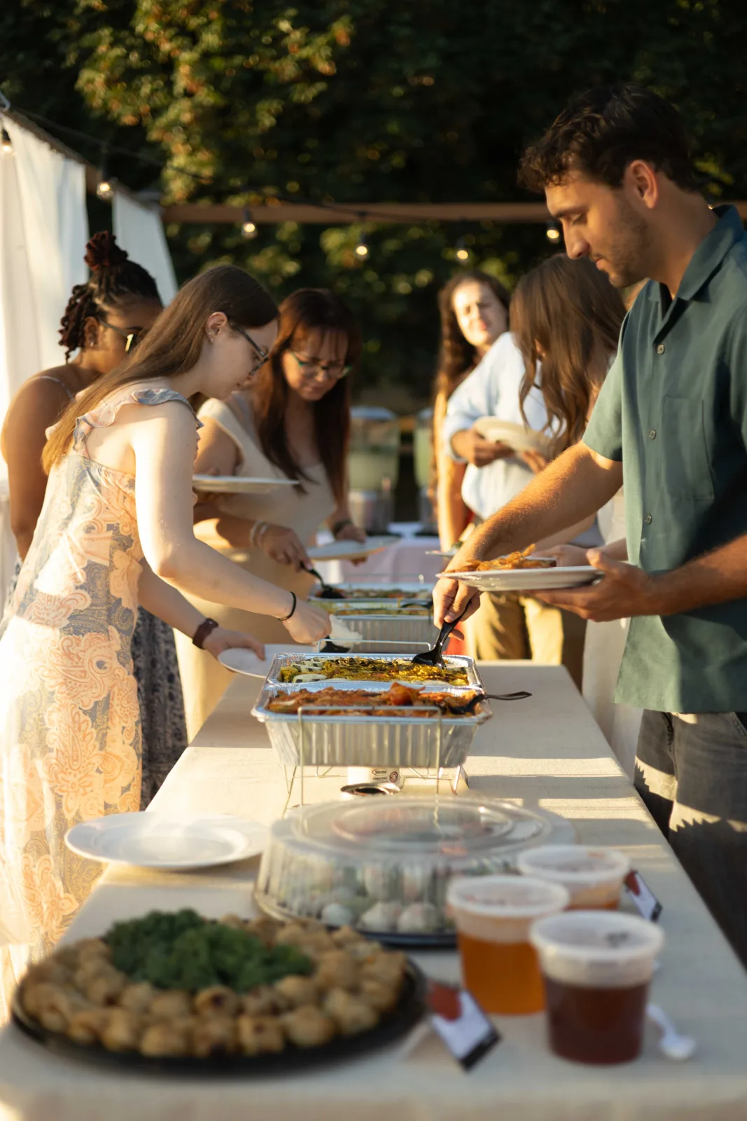 Guests serving themselves at a buffet table in golden evening light