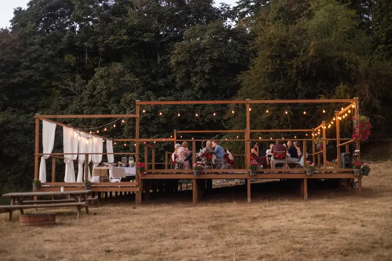Full view of The Porch deck at dusk, lit by string lights, guests seated at long tables